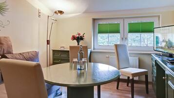 A dining area with a round table, chairs, a vase with flowers, and a window with blinds.