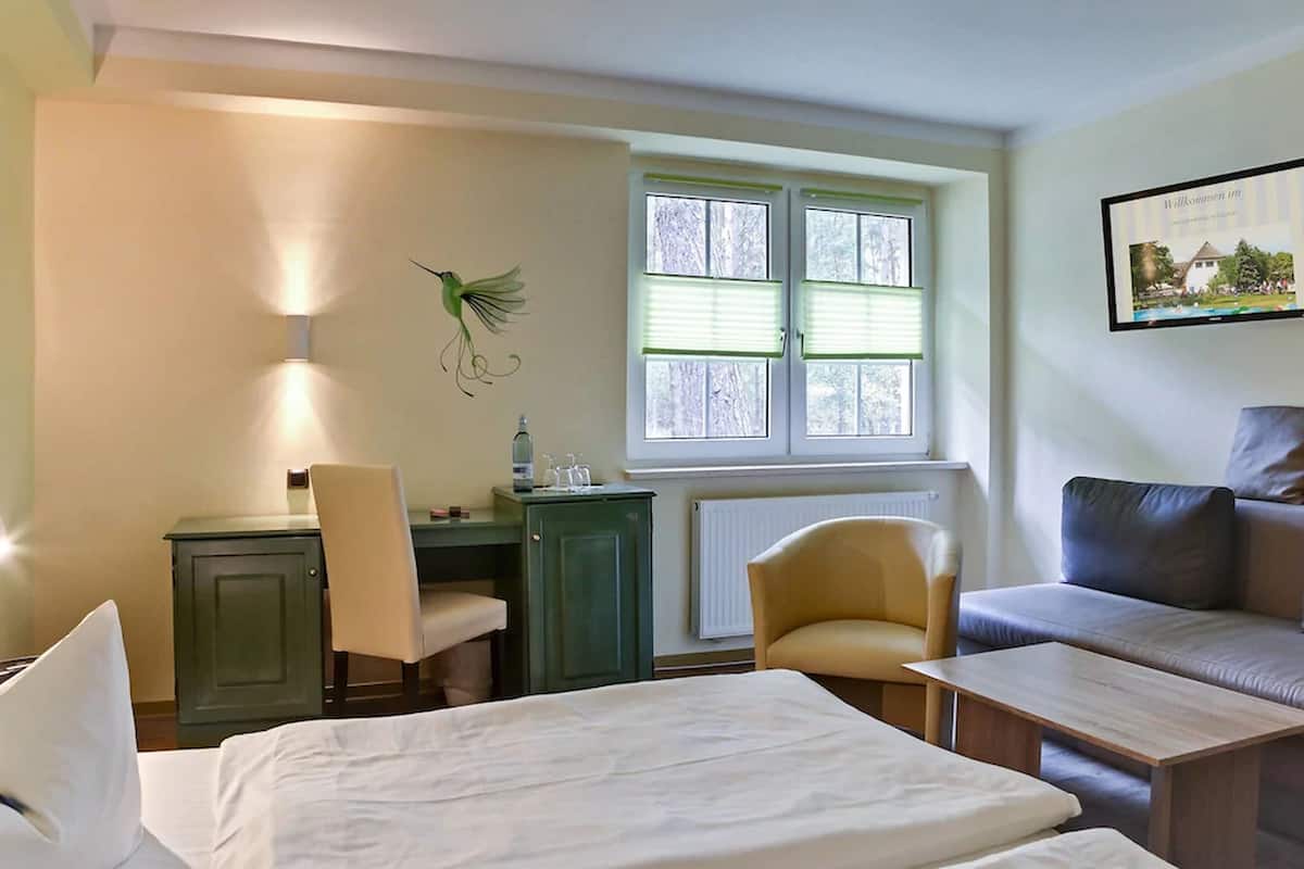 Quarto de hotel com cama, escrivaninha com cadeira, sofá e janela com persianas.