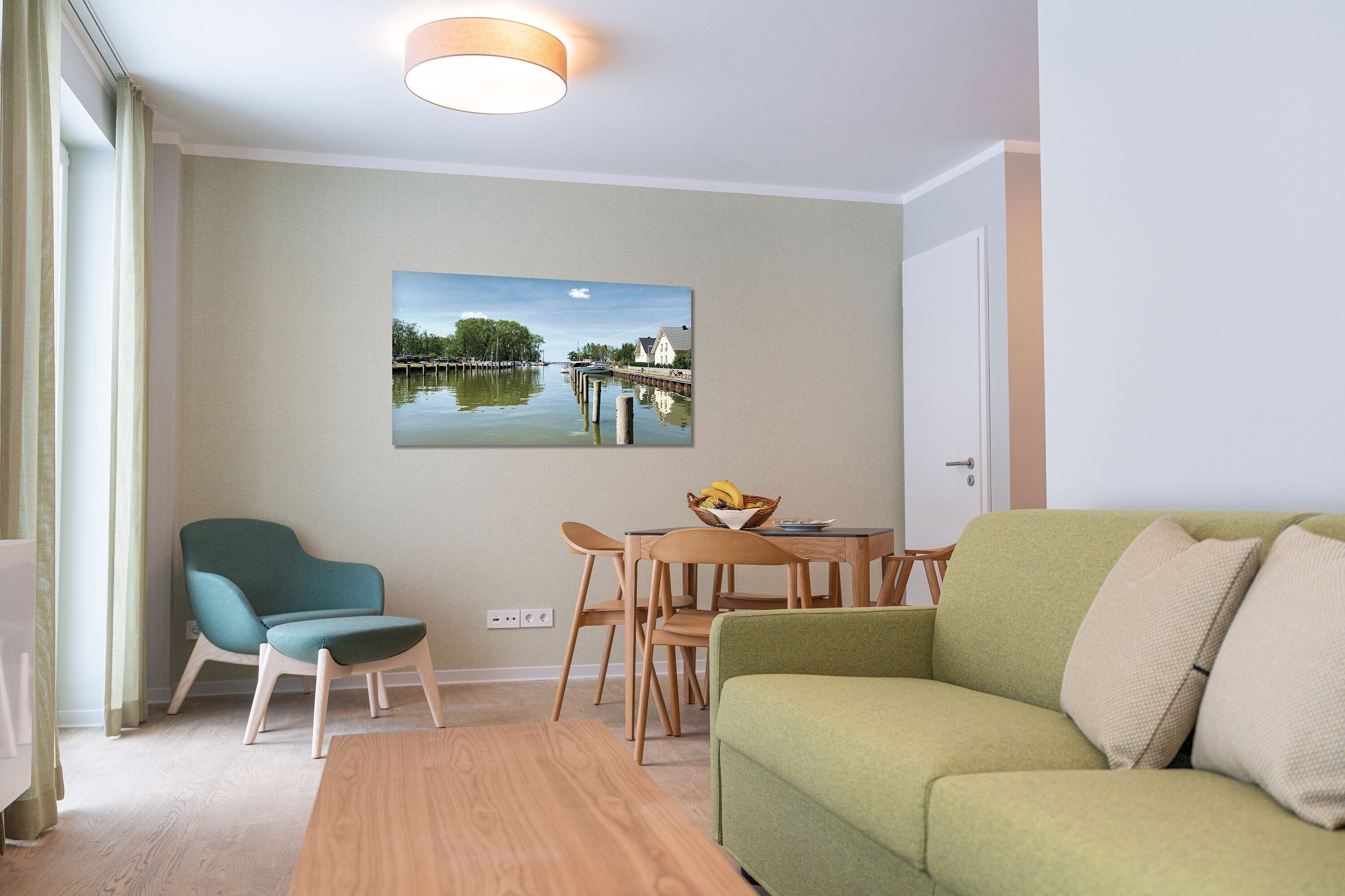 A modern living room with a green sofa, teal armchair, and wooden dining table with chairs. A painting of a water scene is on the wall.