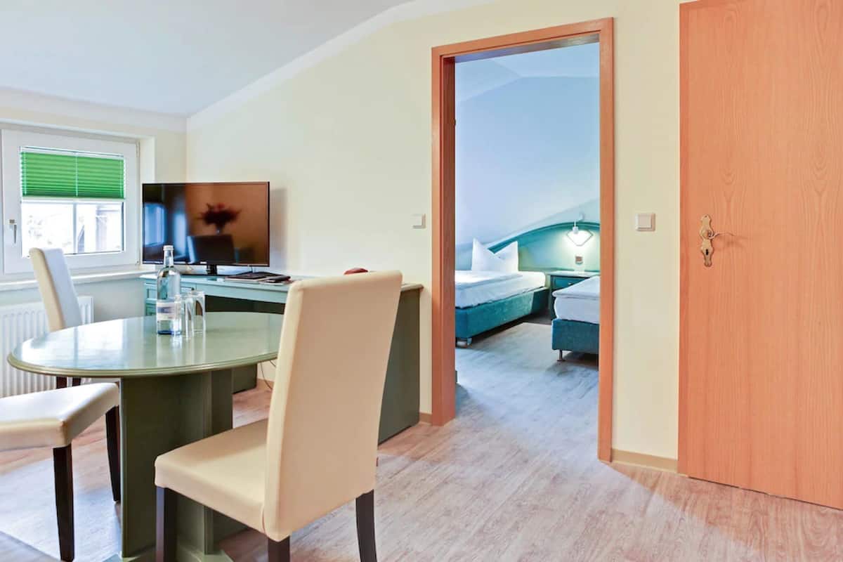 Quarto de hotel com área de refeições, televisão, cama e porta de madeira.