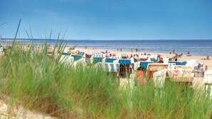 A beach with rows of beach chairs and umbrellas, a sandy foreground with grass, and the ocean in the background. - Familienresort Usedom (Trassenheide)