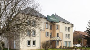Un bâtiment à deux étages, sur lequel on peut lire l’inscription « Mister Bed ». Il est doté d’un toit plat, de nombreuses fenêtres et d’un petit jardin à l’avant.