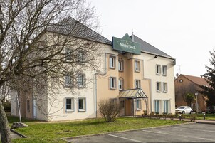 Un bâtiment à deux étages, sur lequel on peut lire l’inscription « Mister Bed ». Il est doté d’un toit plat, de nombreuses fenêtres et d’un petit jardin à l’avant.