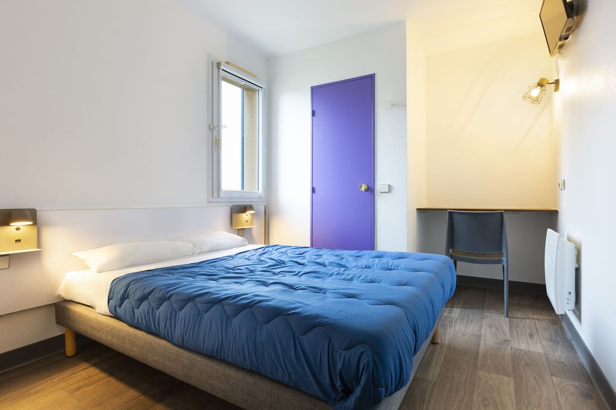 Une chambre à coucher avec un lit, un bureau, une chaise, une fenêtre et une porte.