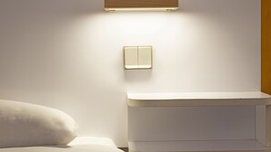 Une salle de bain moderne avec des toilettes blanches, un luminaire fixé au mur et une table de chevet.