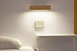 Une salle de bain moderne avec des toilettes blanches, un luminaire fixé au mur et une table de chevet.