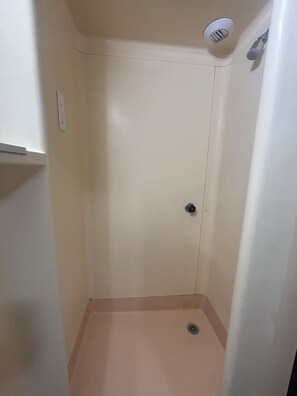 Un espacio de ducha pequeño y cerrado, con un cabezal de ducha, una puerta y un desagüe.