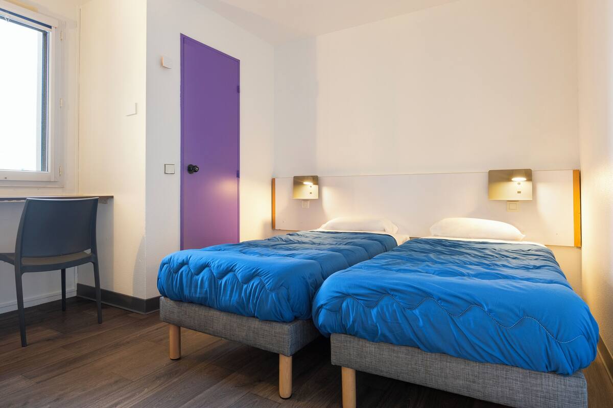 Une chambre avec deux lits, un bureau et une porte violette.