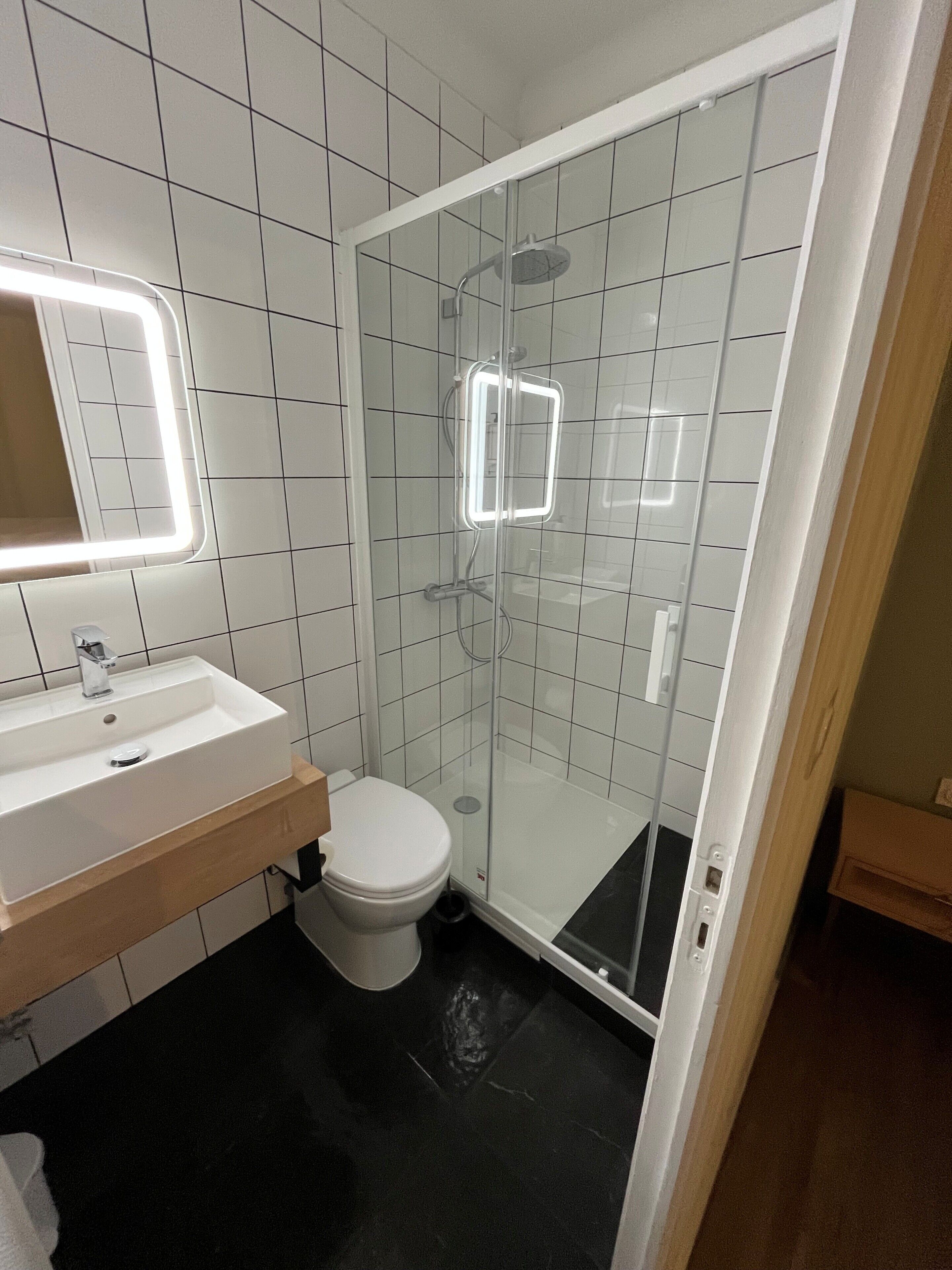 A bathroom with a white sink, a toilet, a glass-enclosed shower, and a mirror with a light.