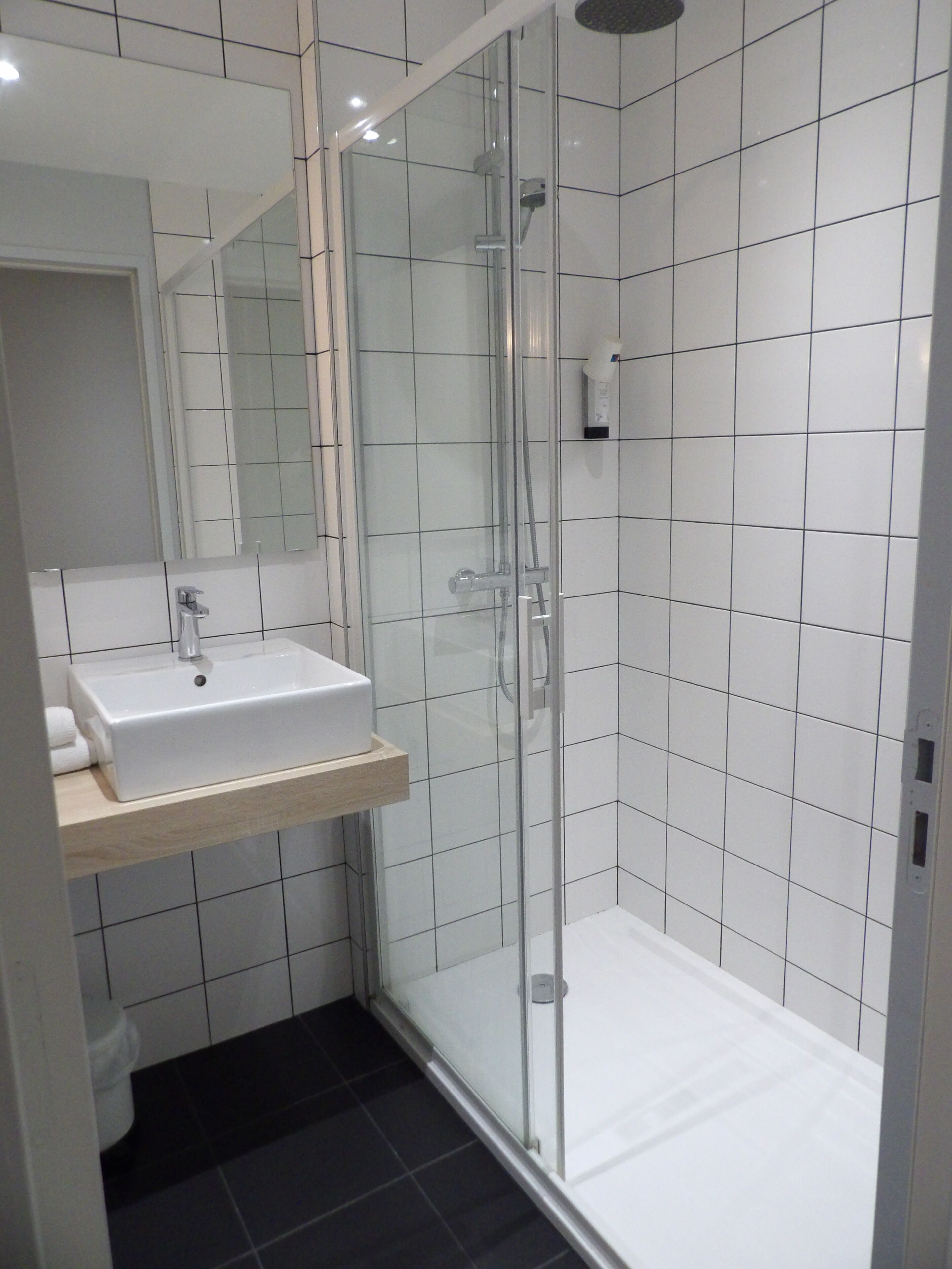 A modern bathroom with a glass-enclosed shower, a white sink with a wooden shelf, and a large mirror.