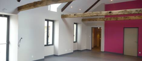 Un interior con vigas de madera expuestas, ventanas amplias y una pared de acento rosa.