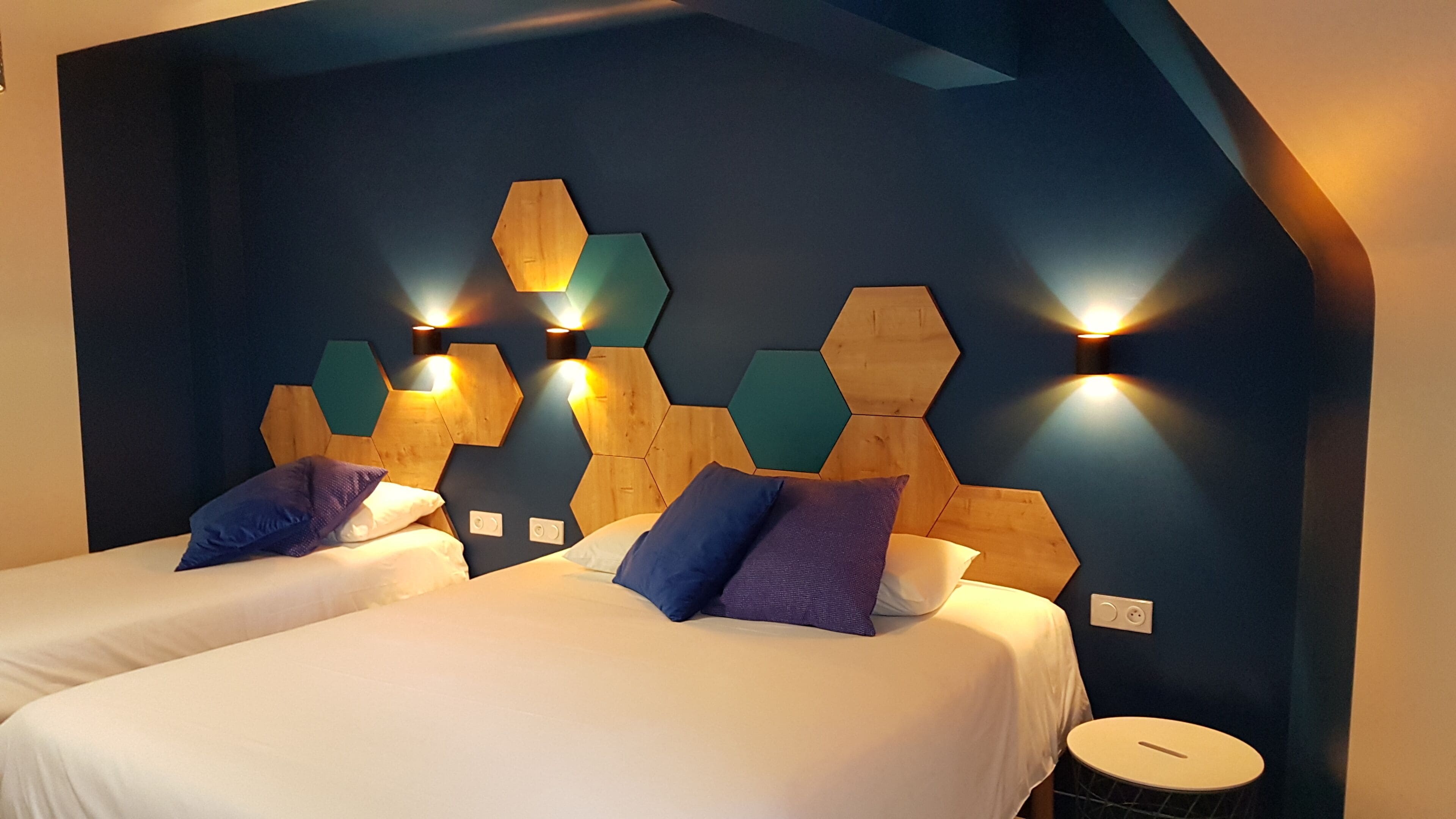 Una habitación de hotel con dos camas, un cabecero geométrico moderno y luces fijadas a la pared.