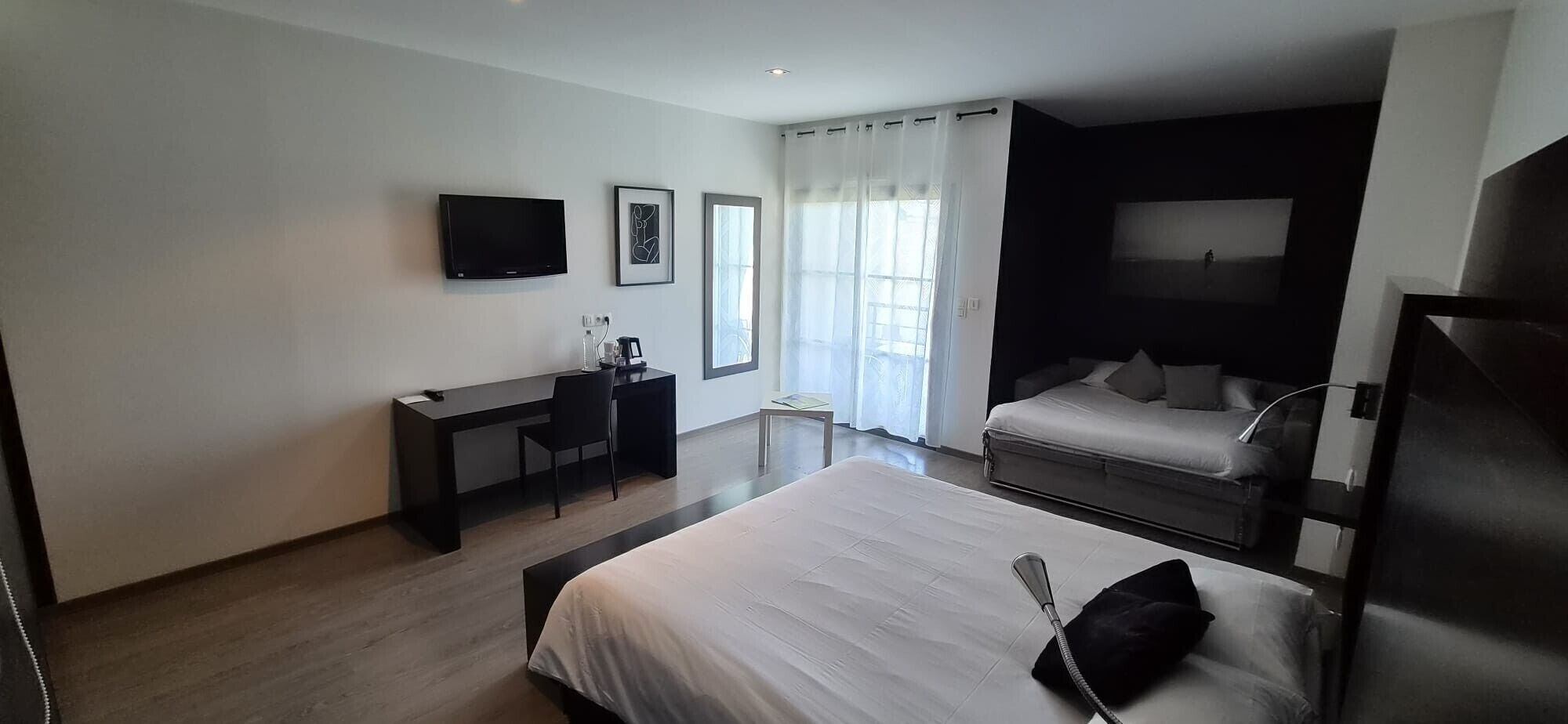 Een moderne hotelkamer met een bed, bureau, stoel, televisie en raam met gordijnen.