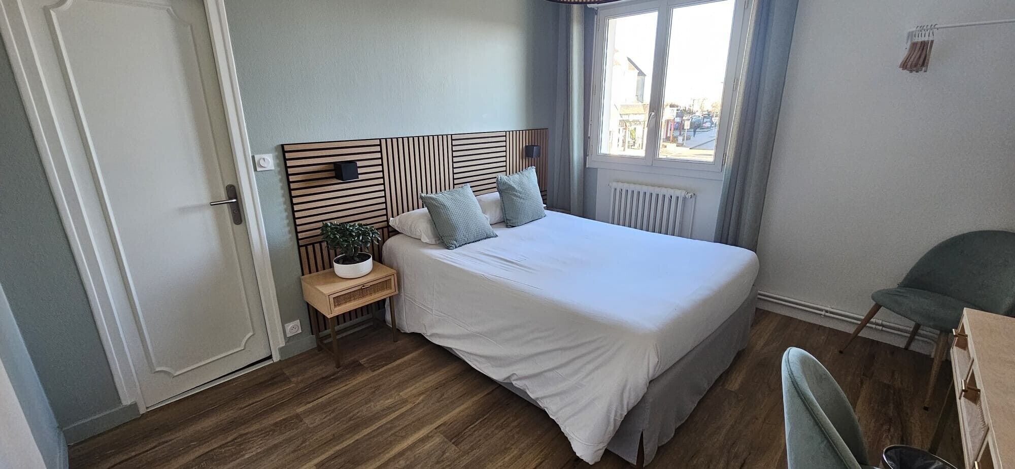 A bedroom with a bed, bedside table, lamp, and a view of the street outside.