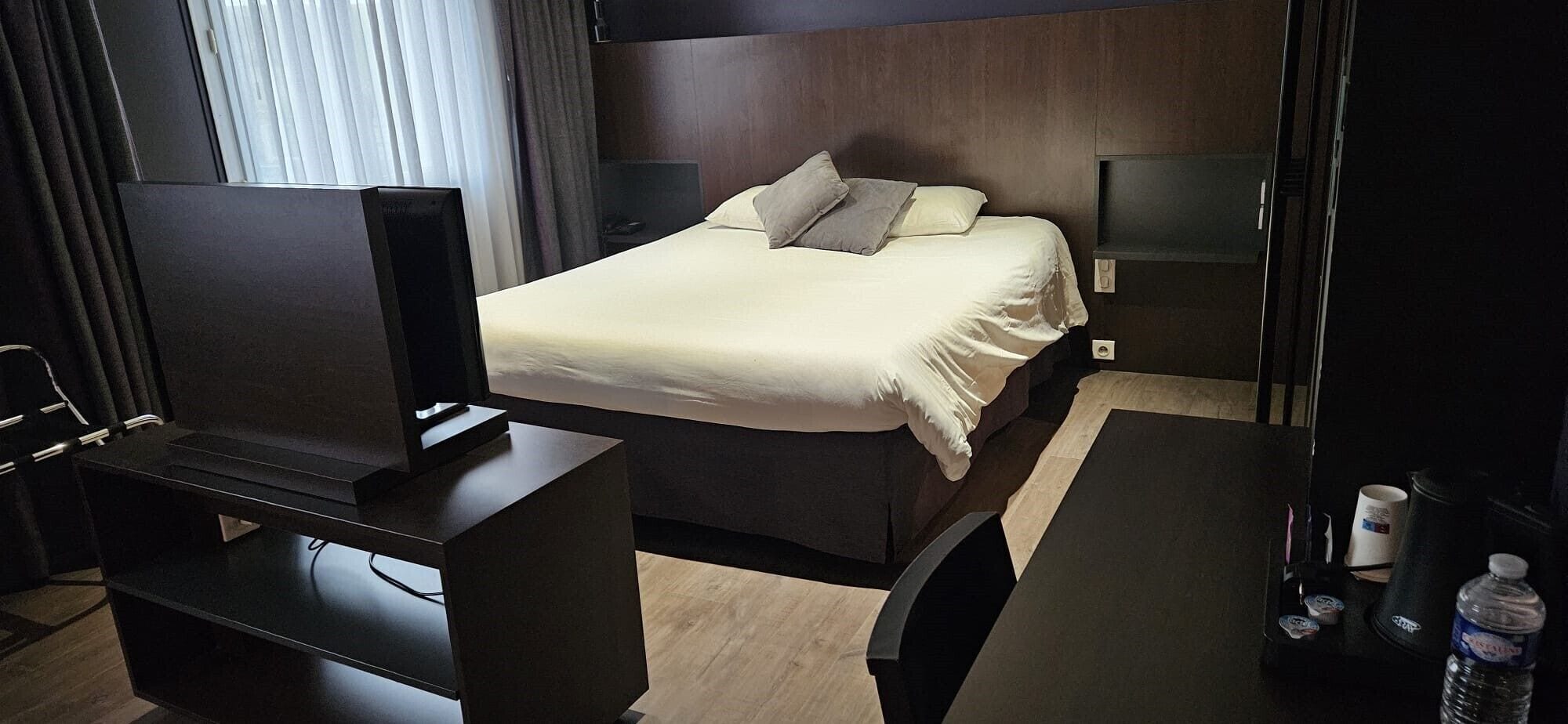 A hotel room with a bed, bedside tables, a TV, and a water bottle.
