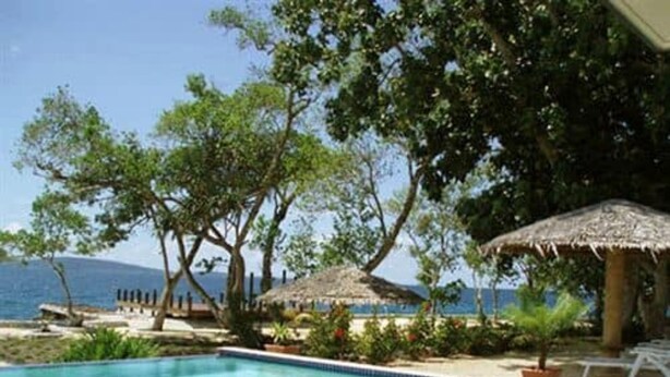 A pool area with a wooden deck, white lounge chairs, and a view of the sea. - Island Magic Resort (Mele)