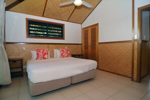Un dormitorio con cama, cabecera de madera, ventana con persianas, ventilador de techo y una puerta.