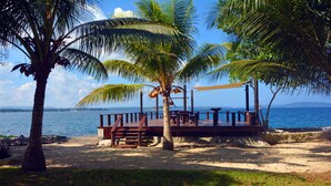 A beach with a wooden deck, palm trees, and a view of the ocean. - Island Magic Resort (Mele)