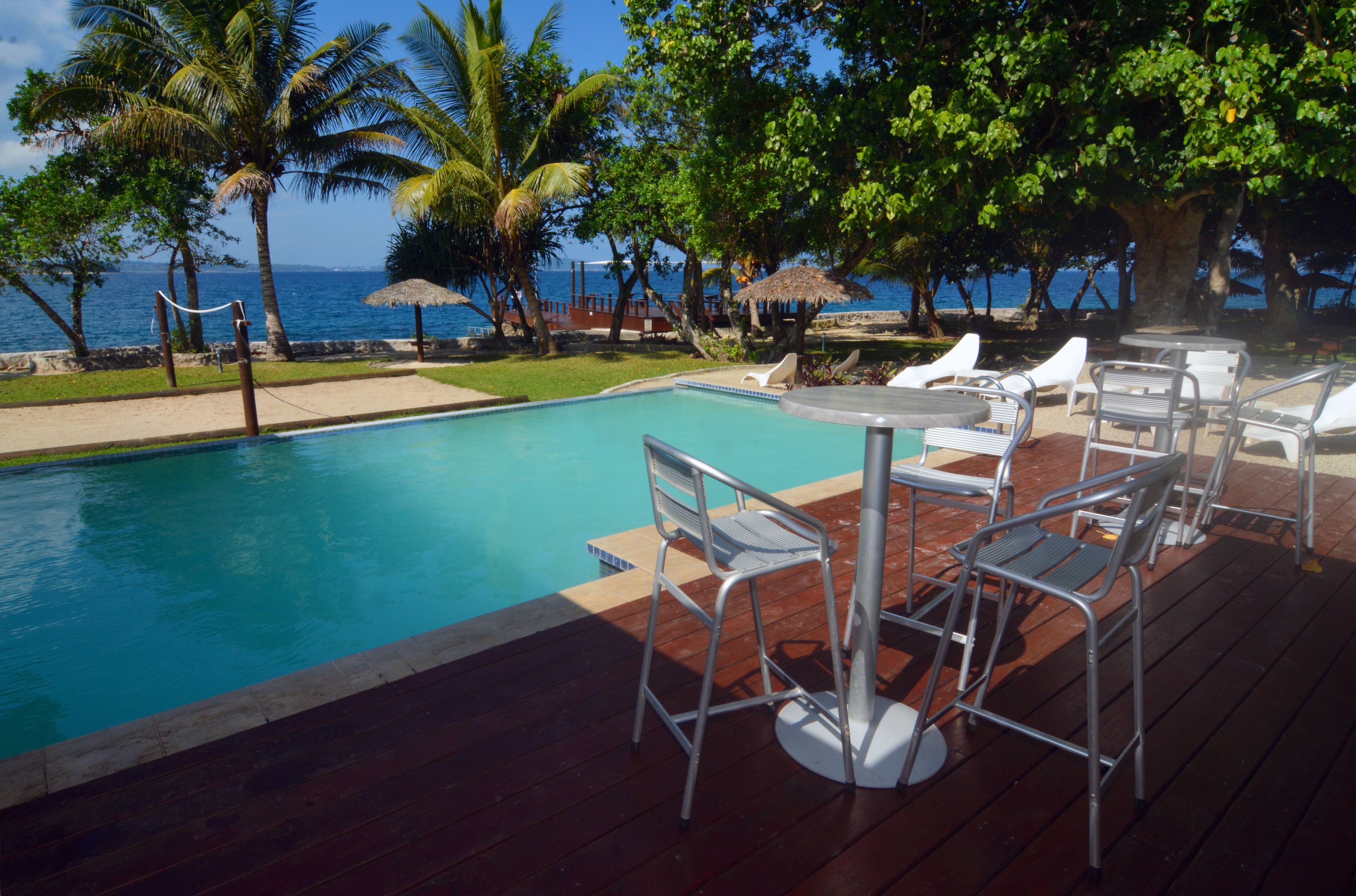 A poolside area with a wooden deck, metal chairs, and a table.