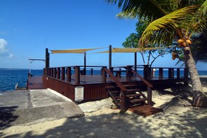Terraza de madera con una palmera y un cartel que advierte sobre una rampa resbaladiza.