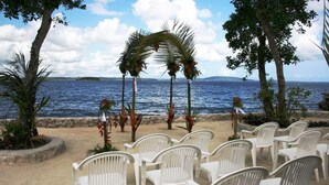 A beachside seating area with white plastic chairs and a palm tree archway. - Island Magic Resort (Mele)