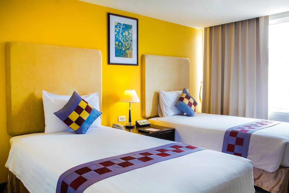 A hotel room with two beds, a nightstand with a lamp, a framed picture on the wall, and a window with curtains.