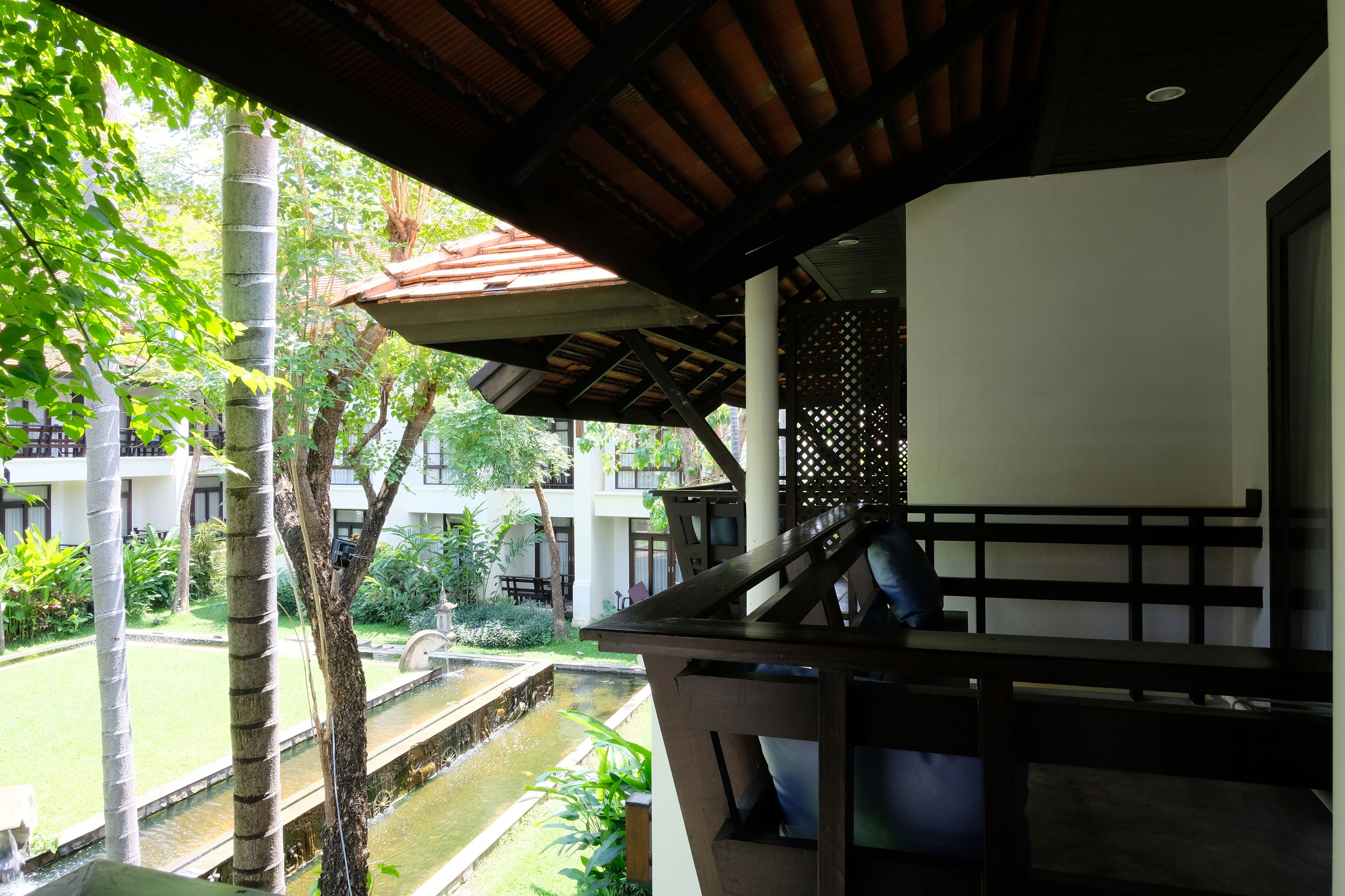 A covered outdoor area with a water feature, wooden benches, and a view of a building with multiple windows.