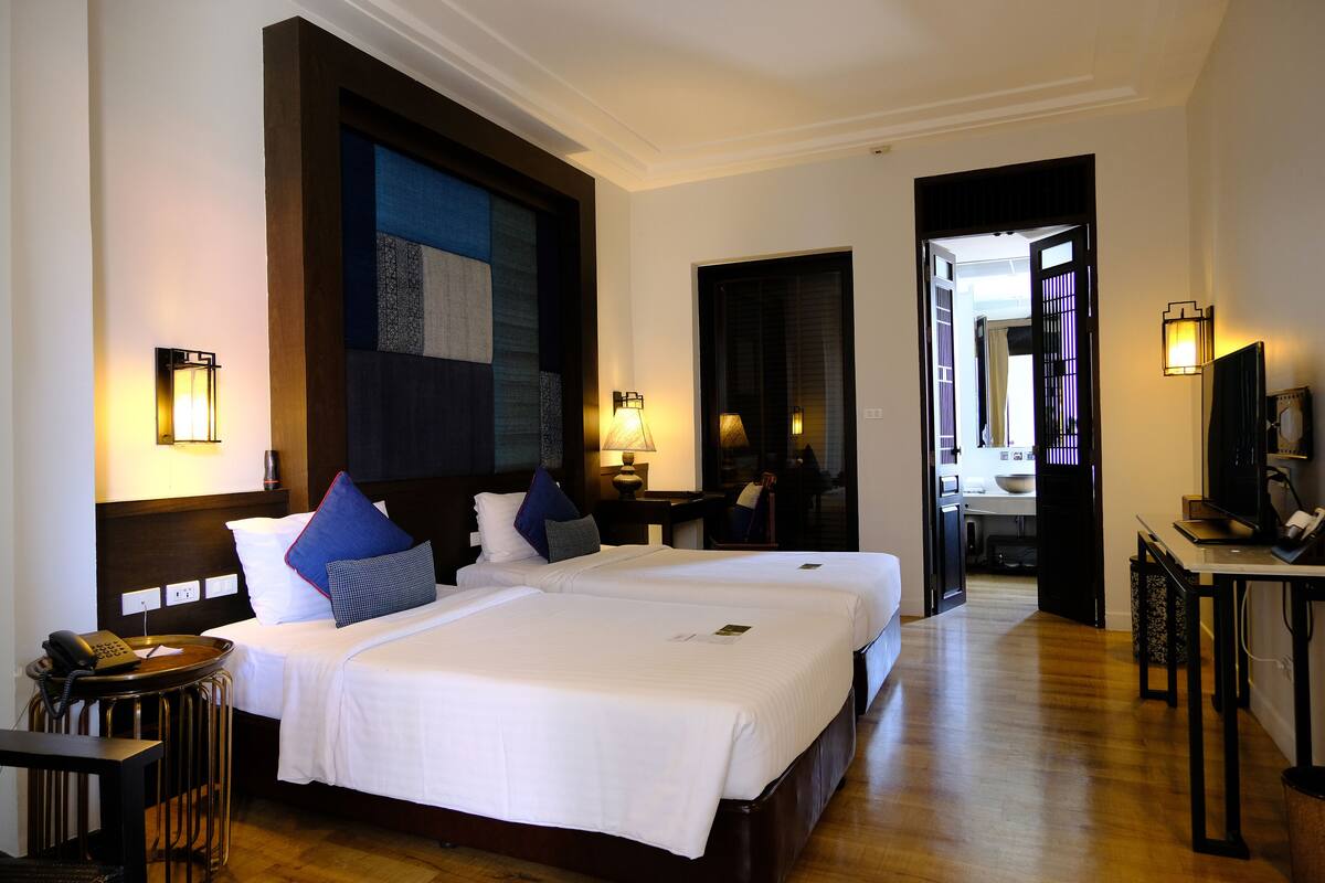 A hotel room with two beds, a desk, a chair, a telephone, and a television.