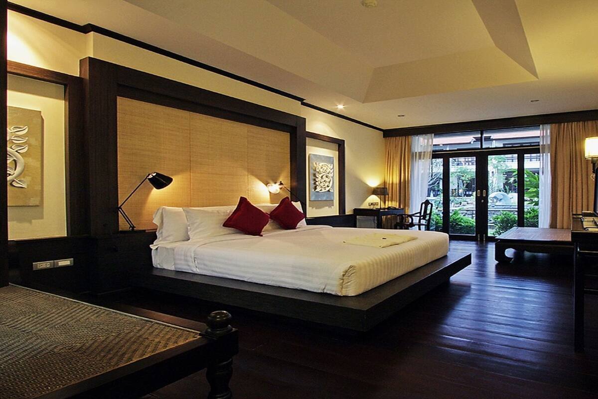 A hotel room with a large bed, bedside lamps, a desk, and a view of greenery outside.