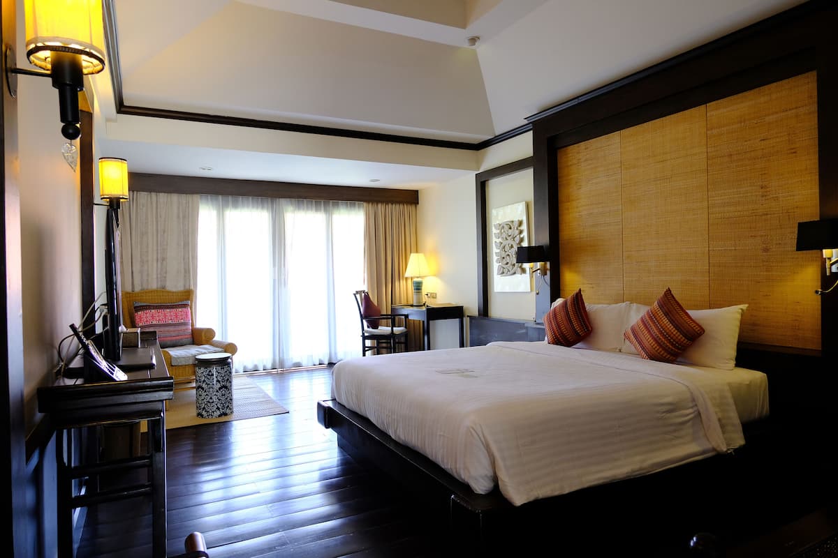 A hotel room with a large bed, a desk with a lamp, a chair, and a small table.
