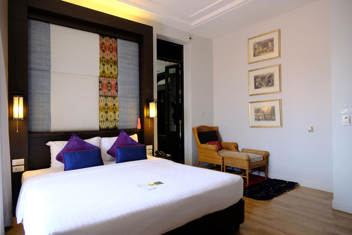 A hotel room with a large bed, a chair, and a wall with framed pictures.