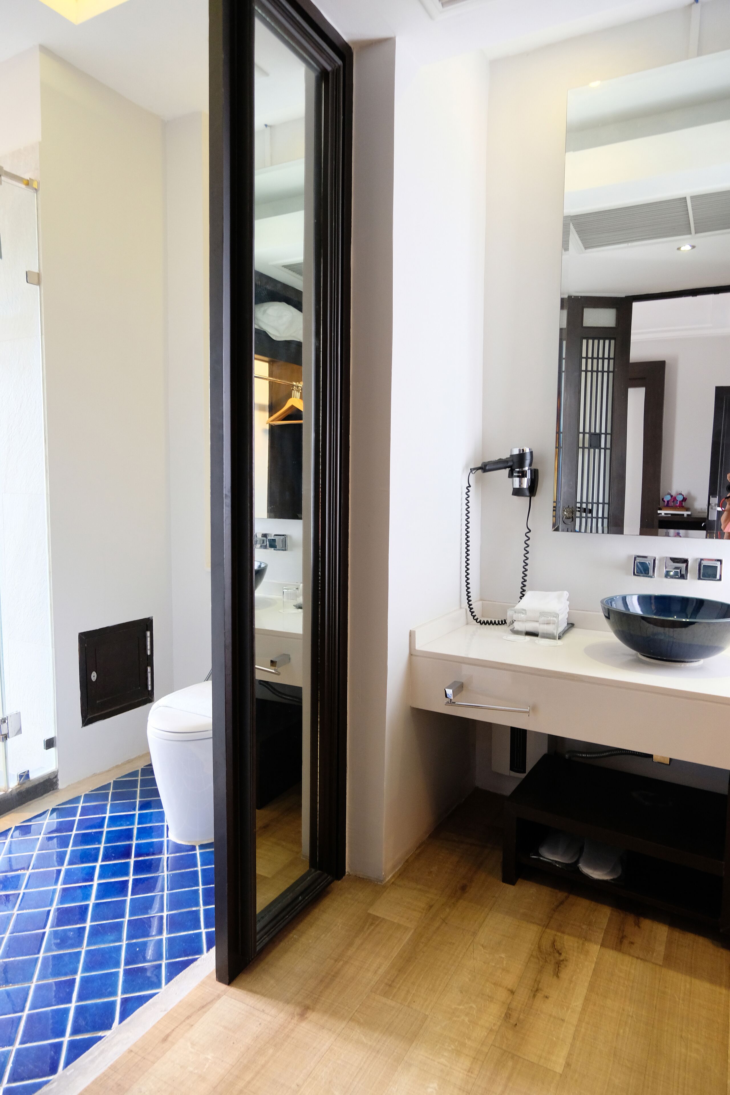 Een moderne badkamer met een grote spiegel, een witte wastafel en een vloer betegeld met blauwe tegels.