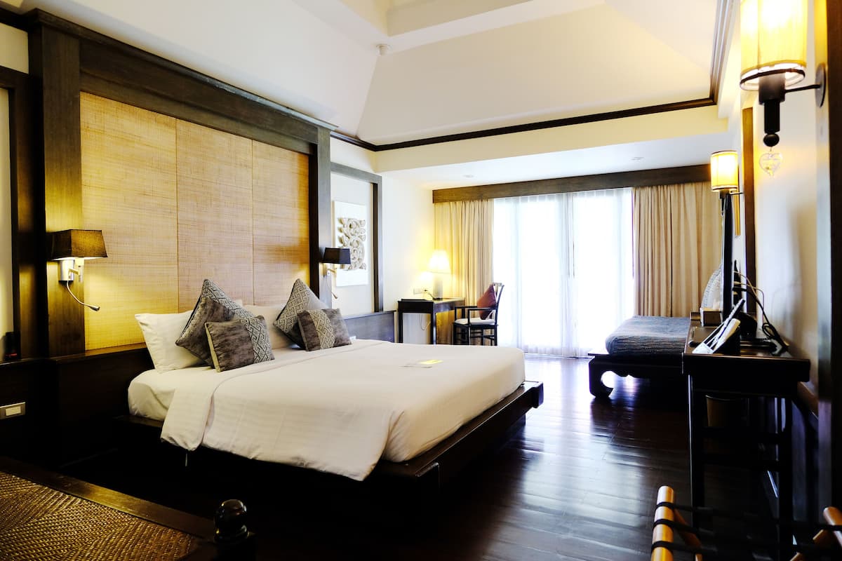 A hotel room with a large bed, a desk, a chair, and a window with curtains.