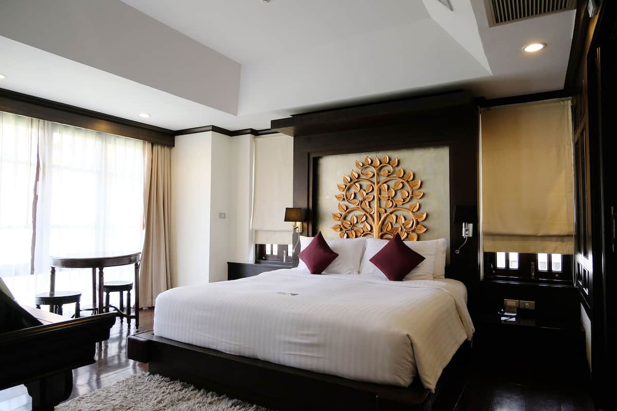 A spacious hotel room with a large bed, a piano, a desk, and a view of the city.