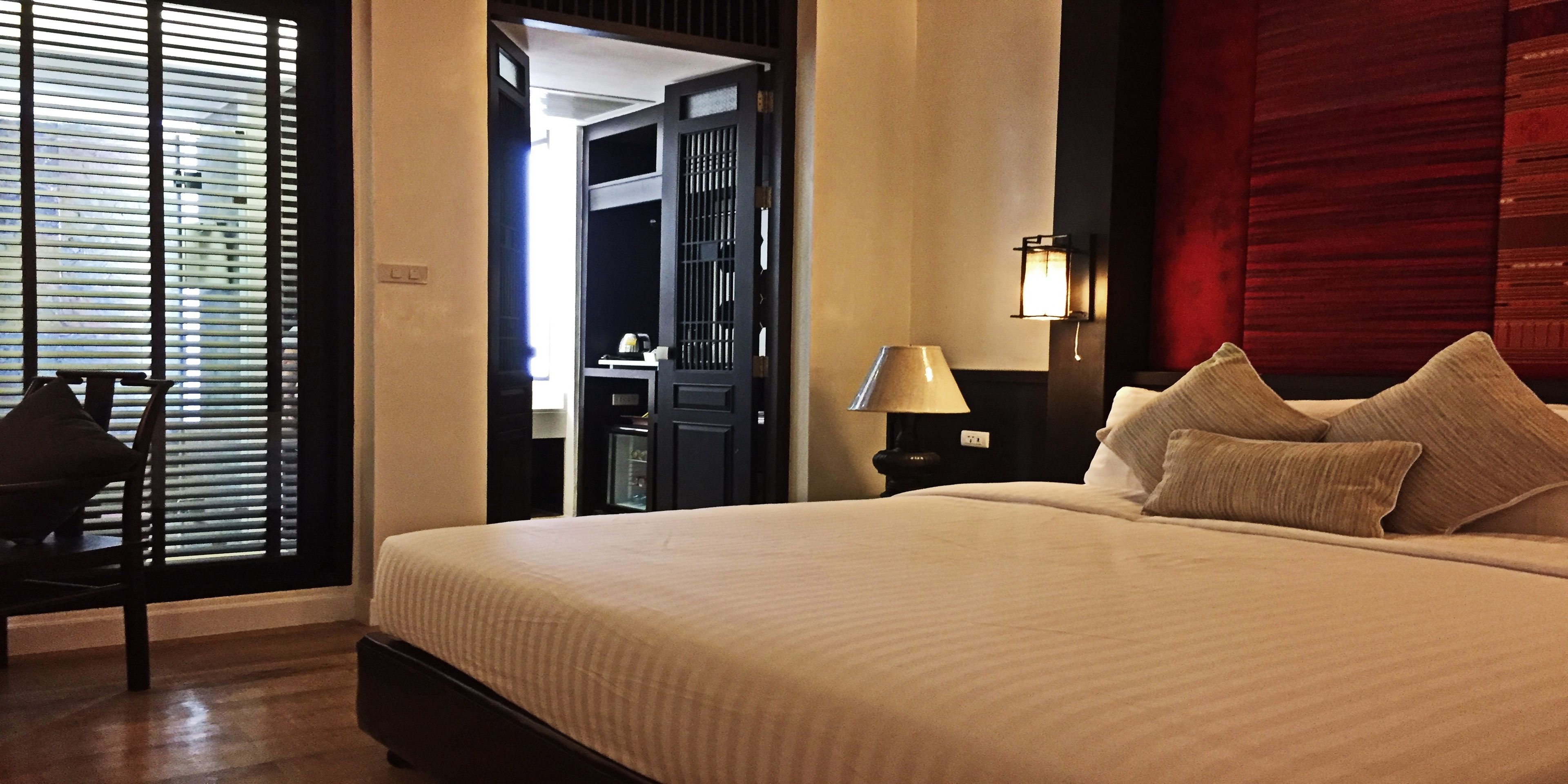Une chambre d’hôtel avec un grand lit, une table de chevet avec une lampe, une chaise et une armoire.