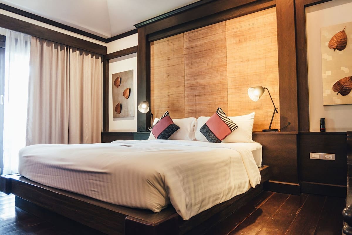 A neatly made bed with a wooden headboard, a bedside table with a lamp, and a framed leaf artwork on the wall.