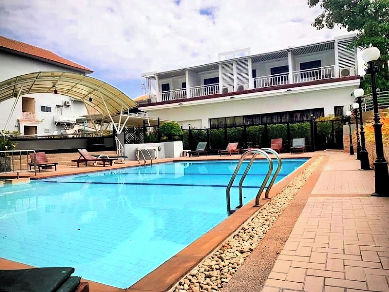 A swimming pool with lounge chairs, a covered area, and a building with multiple balconies.