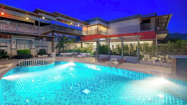 Une piscine dotée d’une plage carrelée, entourée d’un immeuble à plusieurs étages avec des balcons et des espaces de détente en plein air.