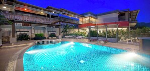 A swimming pool with a tiled deck, surrounded by a multi-story building with balconies and outdoor seating. - Tanawit Hotel Hua Hin (Hua Hin)