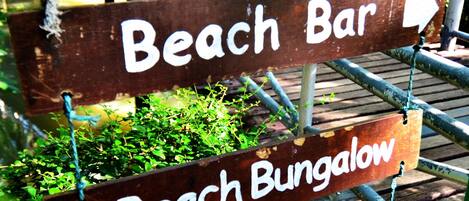 A wooden sign with directions to a Beach Bar and a Beach Bungalow, including numbers 734, 21, 735, and 763.