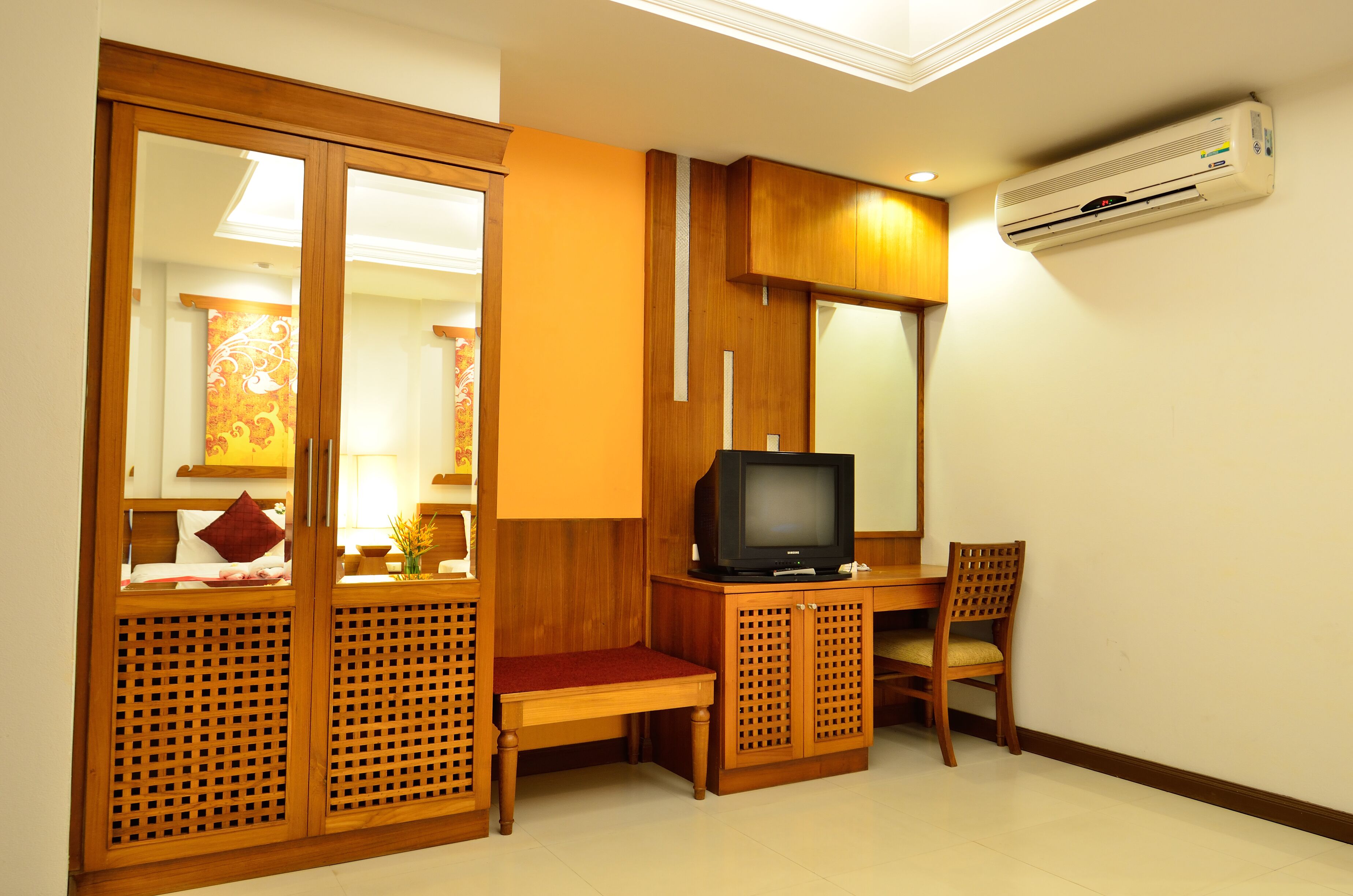 A compact room with a wooden desk, a television, and a chair. An air conditioning unit is mounted on the wall.