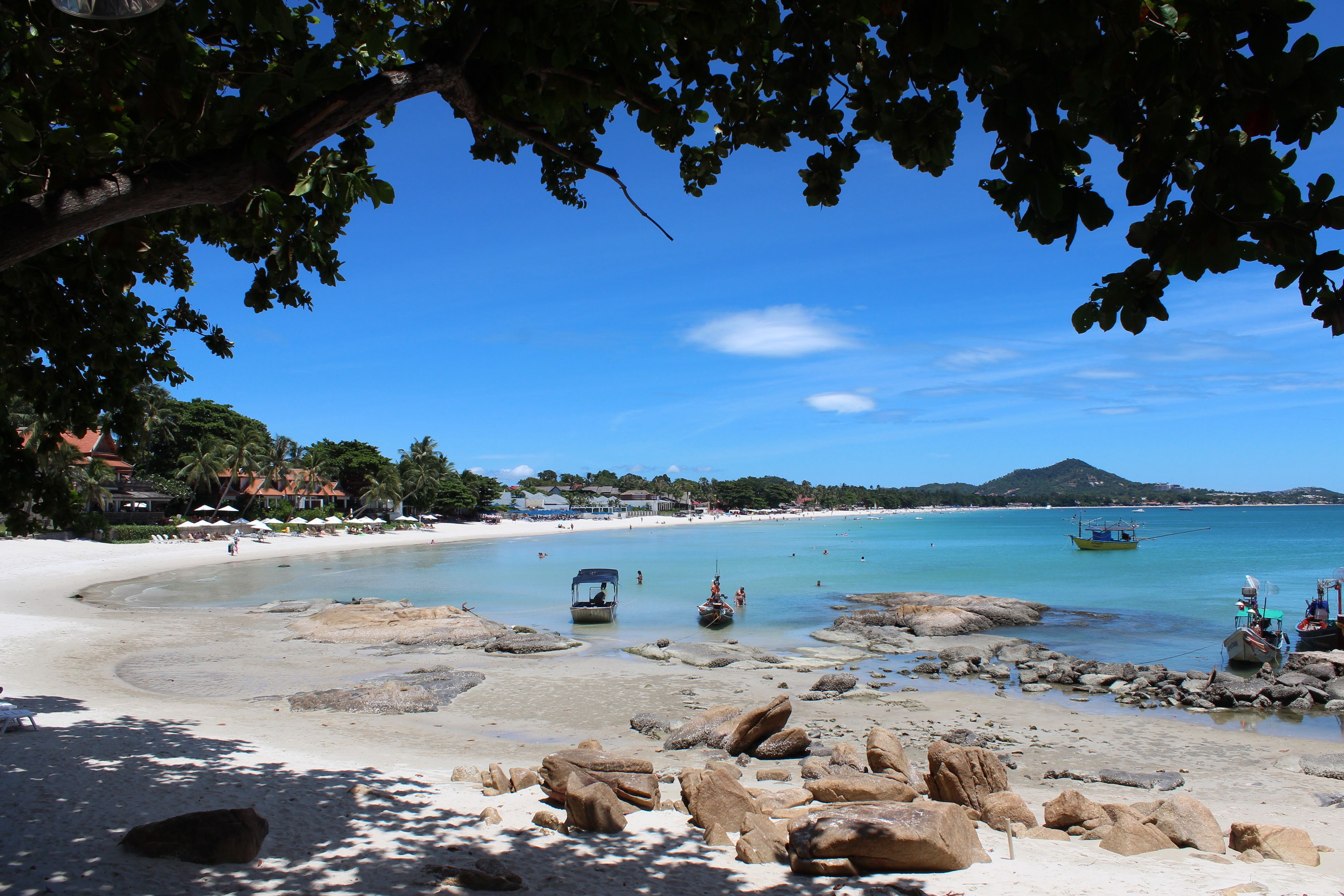 A beach with clear blue water, rocky areas, and a boat.