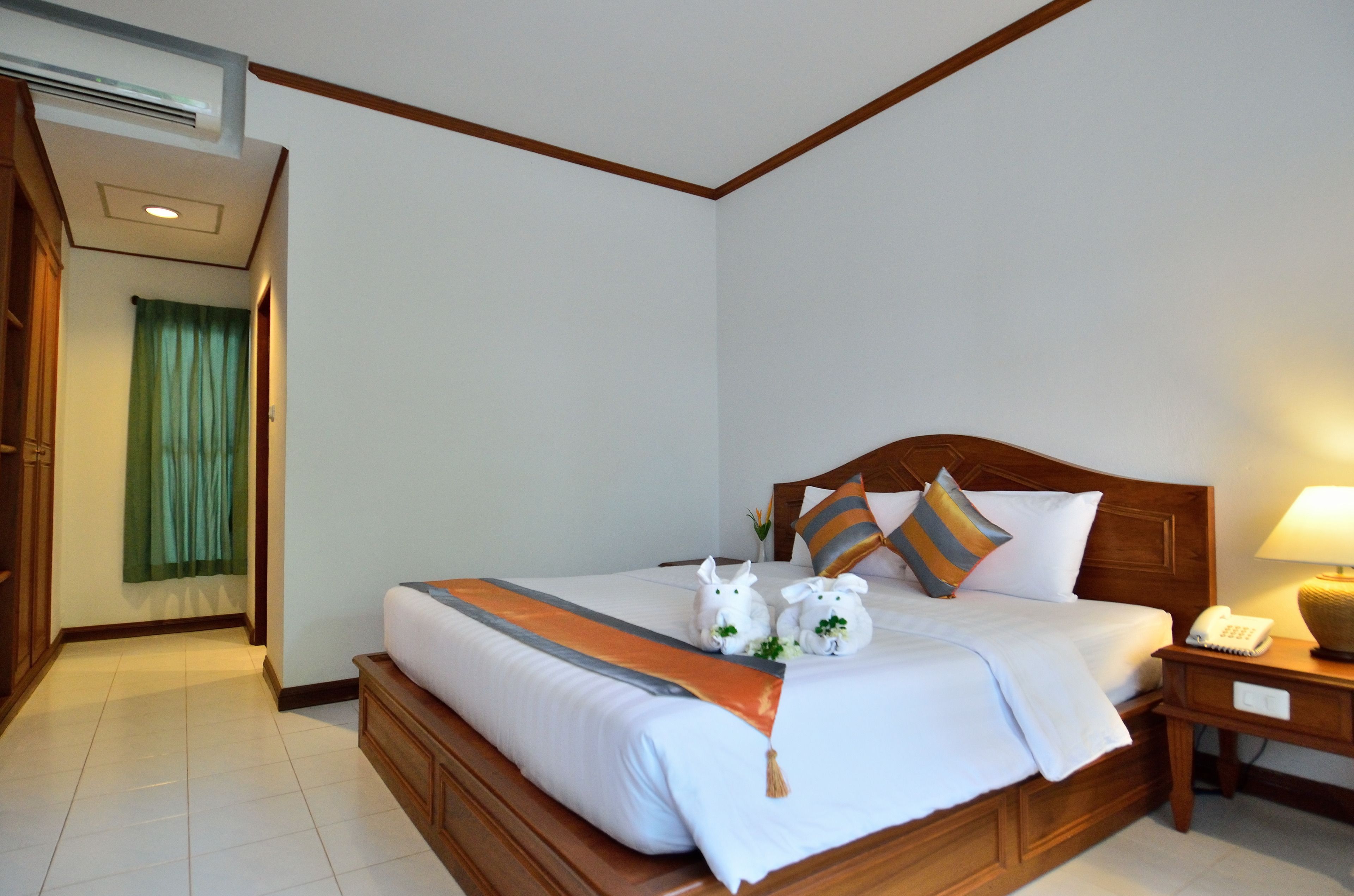 Een hotelkamer met een houten bed, wit beddengoed en twee witte decoratieve objecten die op konijnen lijken.