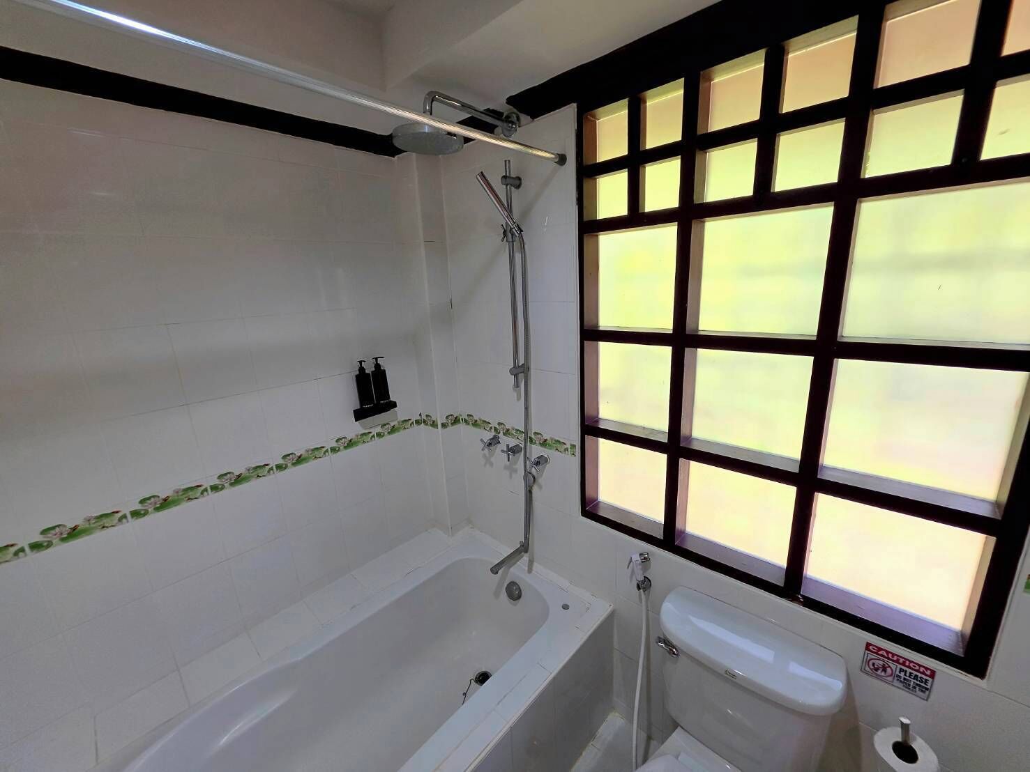 Un baño con bañera, ducha, inodoro y ventana con diseño de cuadrícula.