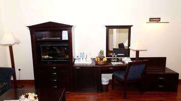 A hotel room with a wooden desk, a chair, a small trash bin, a desk lamp, a mirror, and a television.