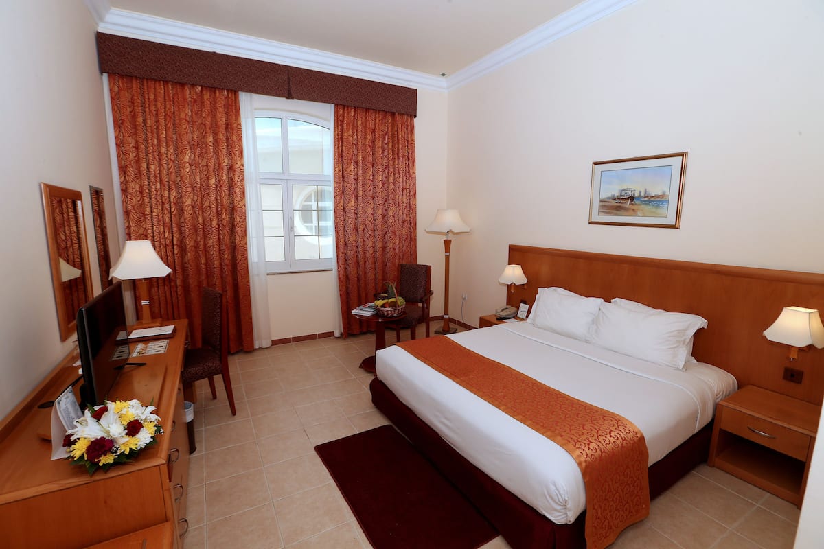 Ein Hotelzimmer mit Bett, Schreibtisch, Stuhl, Lampen und einem Gemälde an der Wand.