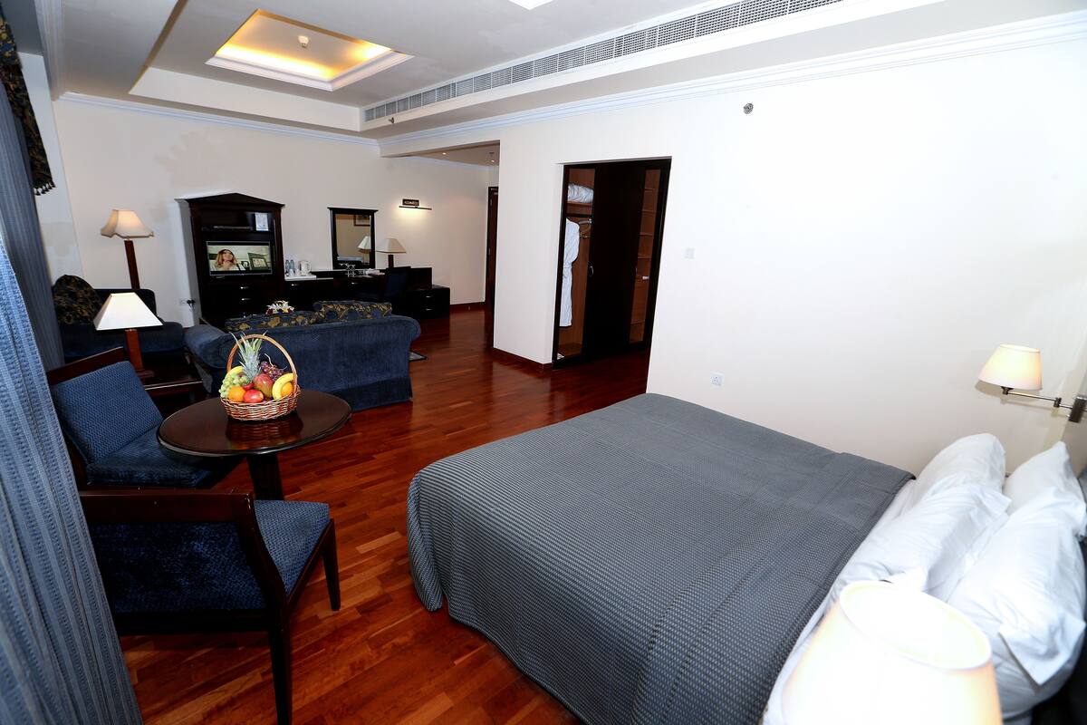 Ein Hotelzimmer mit Bett, Sofa, einem kleinen Tisch mit Obstkorb, Fernseher und Kleiderschrank.