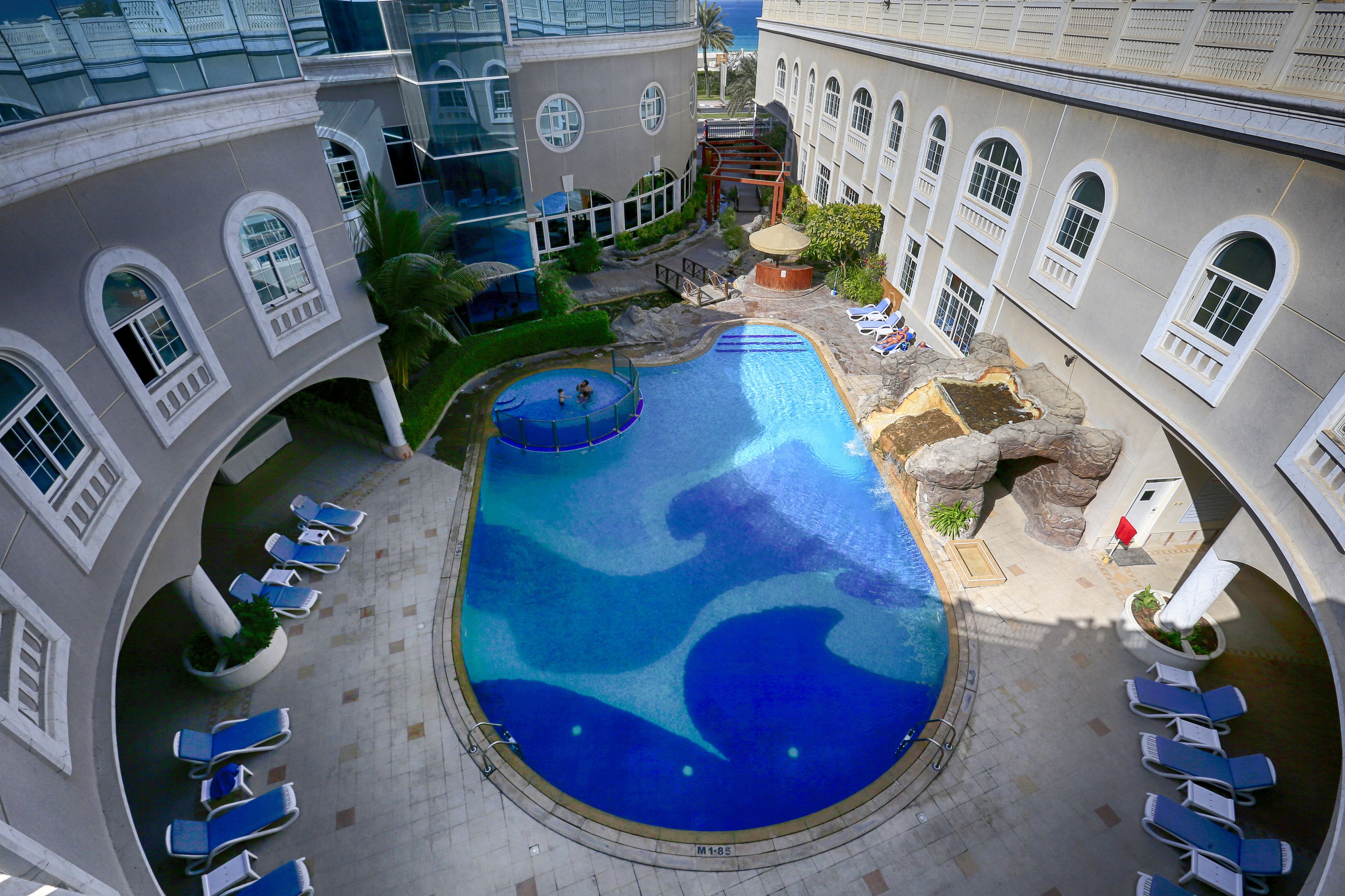 Une piscine sur le toit, avec de l’eau bleue, entourée de chaises longues et agrémentée d’un élément décoratif en roche.