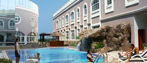 A swimming pool with a waterfall feature, lounge chairs, and a bar area.