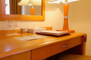Un bureau en bois avec un miroir, une lampe, une boîte de mouchoirs, un carnet et deux verres.